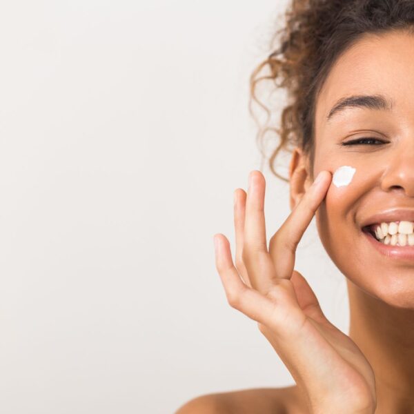 Woman smiling while applying moisturizer to her face with her pointer finger. 