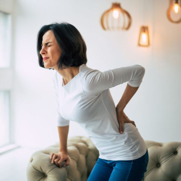 woman bracing herself on a sofa arm while grabbing at her low back in pain