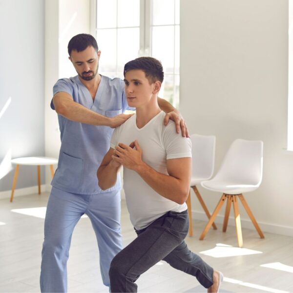 man in light blue scrubs assists another man in stabilized lunge position