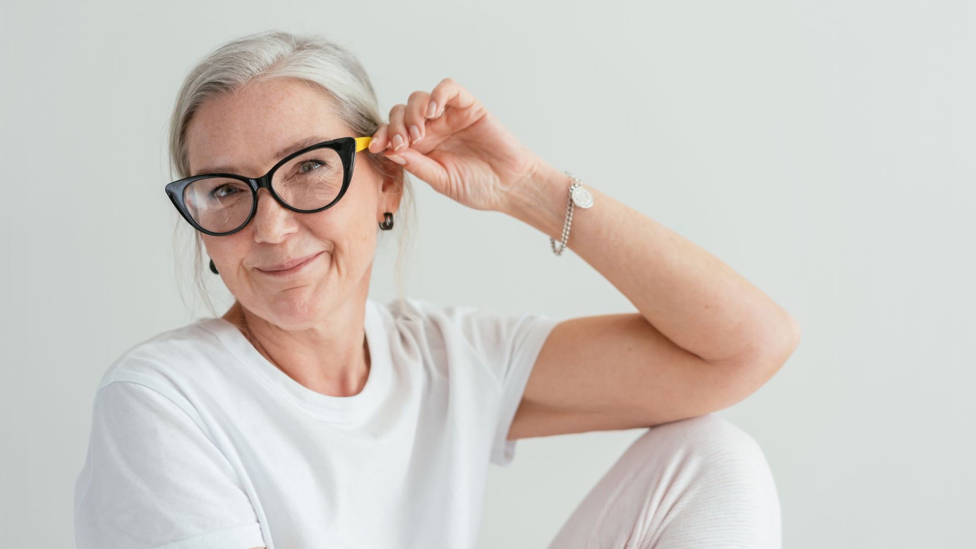 middle age woman in white room sits and hold glasses